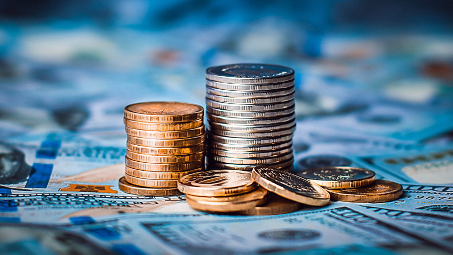 Stacks of coins against the background of hundred-dollar bills are scattered throughout the space. The coins are collected in two columns, they are shiny, golden in color.